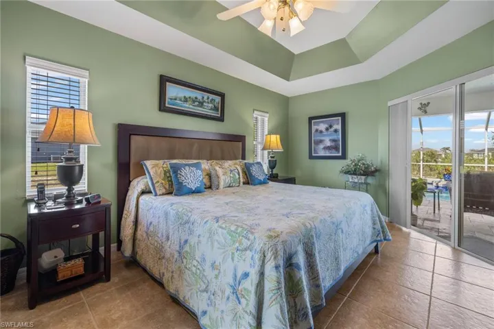 Tiled bedroom with ceiling fan, a raised ceiling, multiple windows, and access to outside