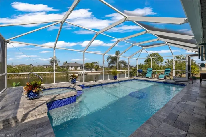 View of swimming pool featuring an in ground hot tub, a water view, glass enclosure, and a patio
