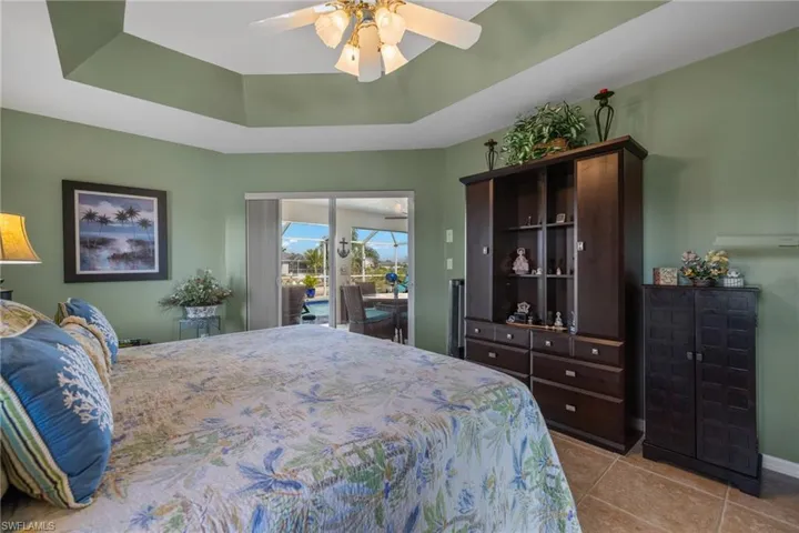 Tiled bedroom with access to outside, a raised ceiling, and ceiling fan