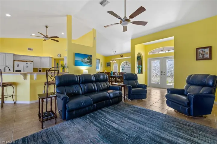 Living room with french doors, tile patterned floors, sink, high vaulted ceiling, and ceiling fan