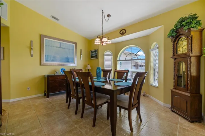 Dining area with light tile patterned flooring, lofted ceiling, and a notable chandelier