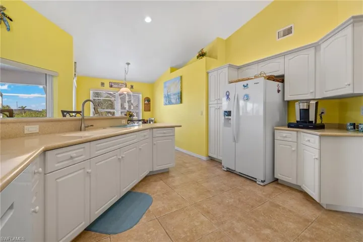 Kitchen with sink, vaulted ceiling, white fridge with ice dispenser, pendant lighting, and white cabinets