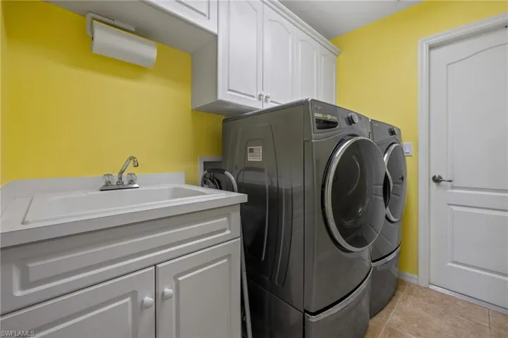 Clothes washing area with light tile patterned flooring, cabinets, separate washer and dryer, and sink