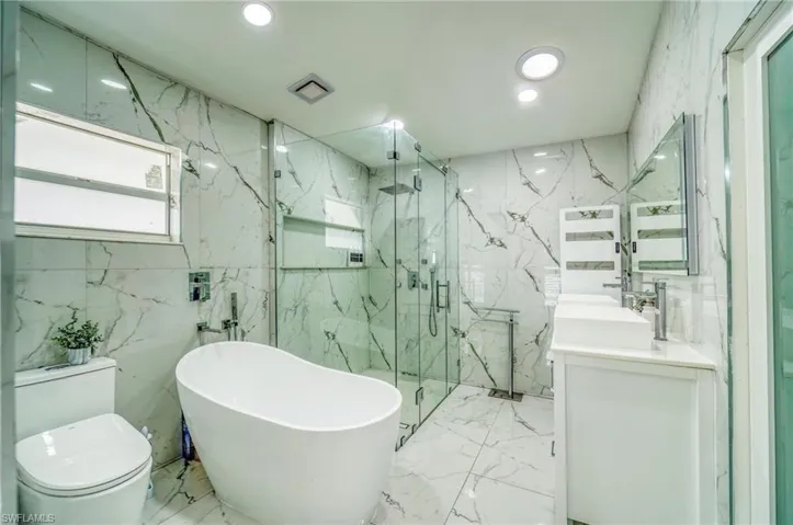 Full bathroom with marble tiled floors, a marble finish shower, toilet, tile walls, and a soaking tub