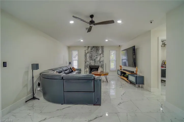 Living area featuring baseboards, a ceiling fan, light marble finish flooring, recessed lighting, and a fireplace