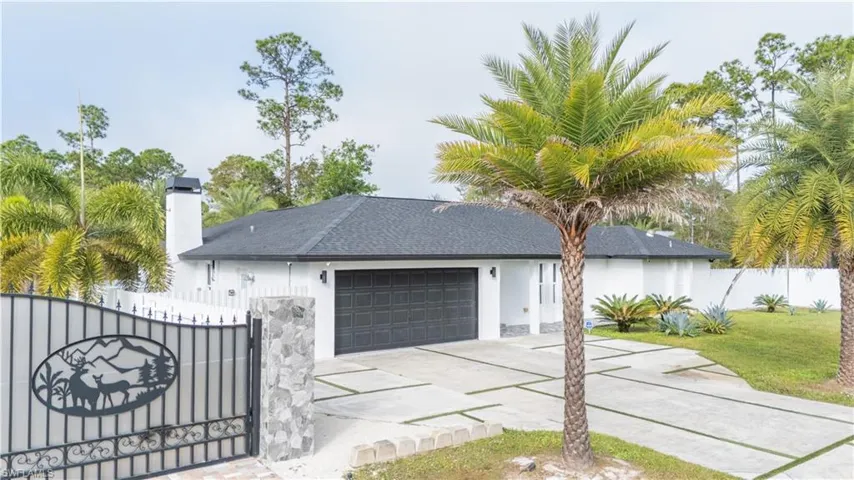 View of front facade featuring a garage, driveway, a chimney, a gate, and stucco siding