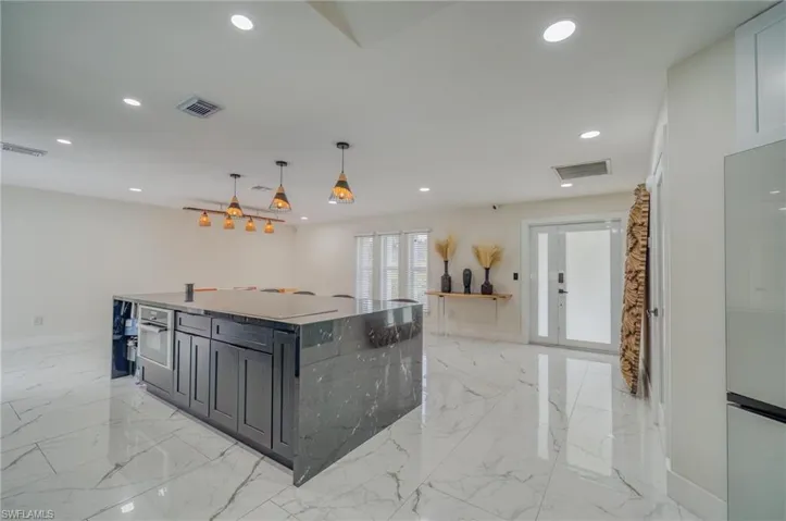 Kitchen with stainless steel oven, light marble finish floors, recessed lighting, dark cabinetry, and baseboards