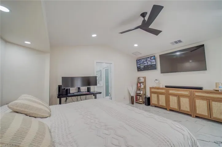 Bedroom featuring recessed lighting, light marble finish flooring, lofted ceiling, a ceiling fan, and ensuite bath