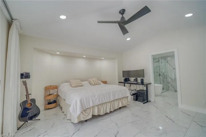 Bedroom with light marble finish floors, recessed lighting, vaulted ceiling, ensuite bathroom, and a ceiling fan