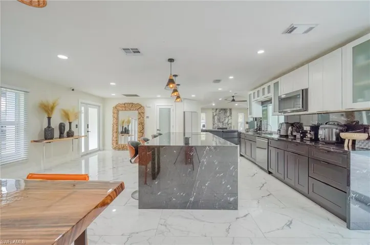 Kitchen with appliances with stainless steel finishes, a kitchen island, dark stone counters, glass insert cabinets, and recessed lighting