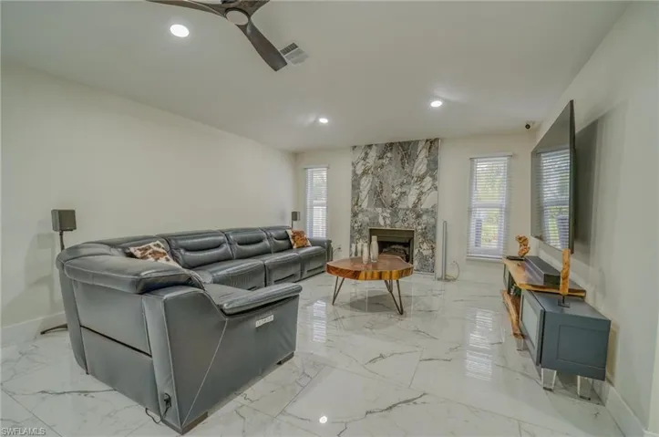 Living room featuring recessed lighting, light marble finish floors, baseboards, a ceiling fan, and a large fireplace