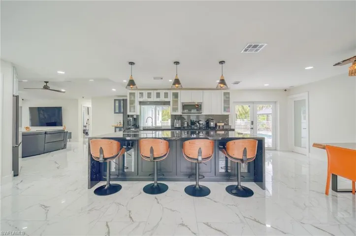 Kitchen with stainless steel microwave, recessed lighting, white cabinets, glass insert cabinets, and light marble finish floors