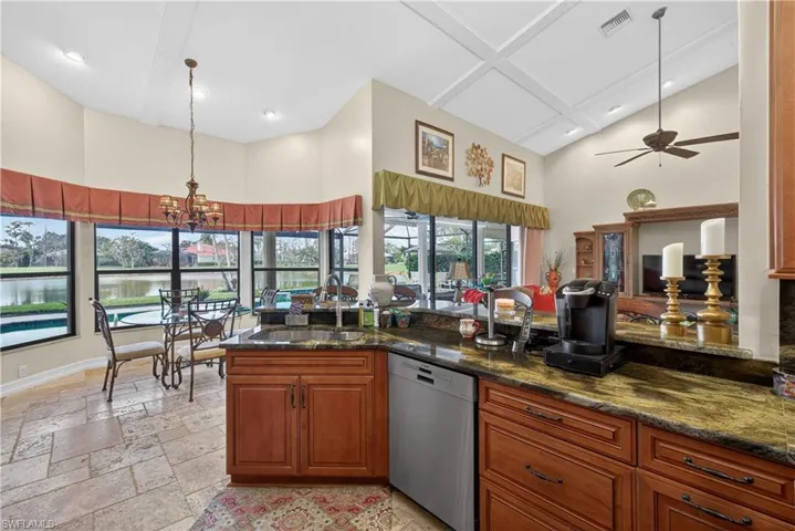 Kitchen with wood finish cabinets, dishwasher, dark stone counters, hanging lights, and stone tile flooring