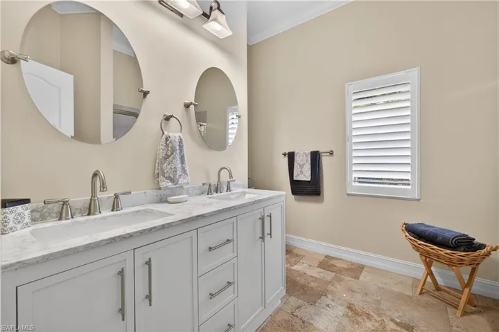 Full bath with ornamental molding, double vanity, and light stone finish flooring