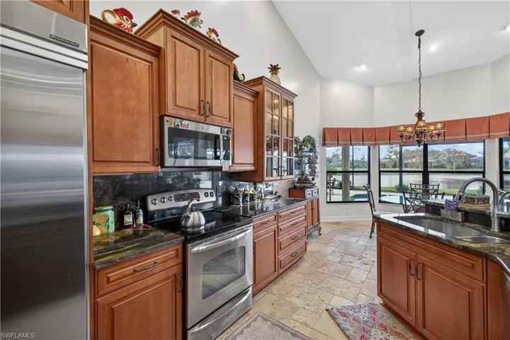 Kitchen featuring stainless steel appliances, wood finish cabinetry, suspended lighting, dark stone counters, and a high ceiling