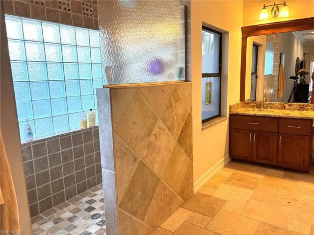 Full bathroom featuring stone tile floors, vanity, and a tile shower