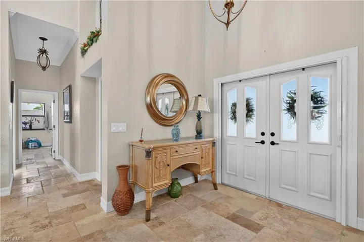 Foyer entrance with a high ceiling, stone tile flooring, hanging lights, crown molding, and french doors