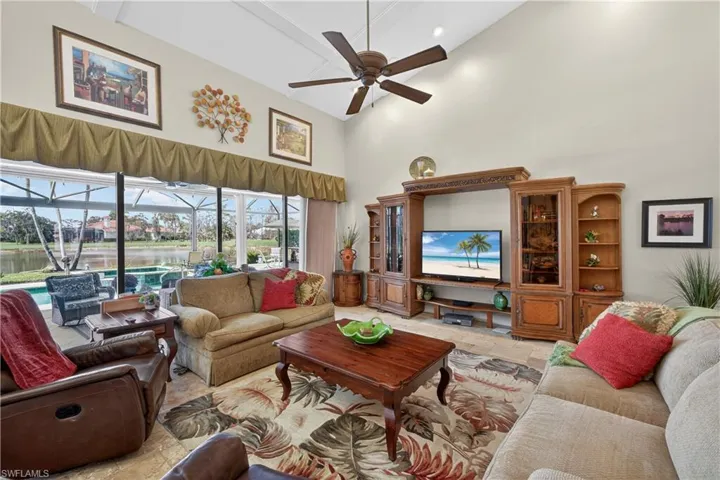 Living area with a sunroom, stone tile flooring, ceiling fan, and lofted ceiling