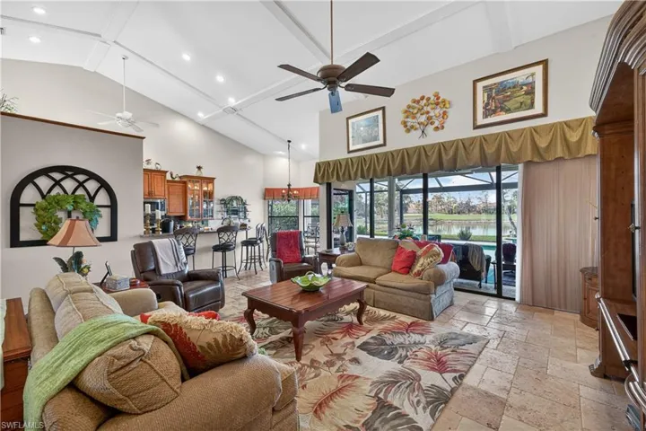 Living area featuring stone tile floors, ceiling fan, vaulted ceiling, a sunroom, and a water view