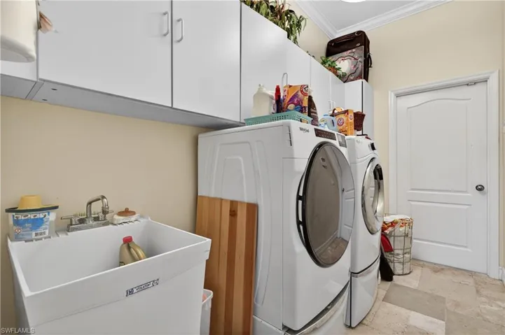 Laundry room with stone finish floors, separate washer and dryer, ornamental molding, and cabinet space
