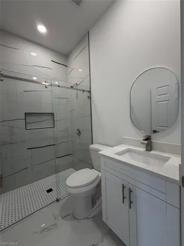 Modern bathroom featuring a glass-enclosed shower with a linear drain, white marble-look wall and floor tiling, a built-in shower niche, and a contemporary vanity with a countertop sink