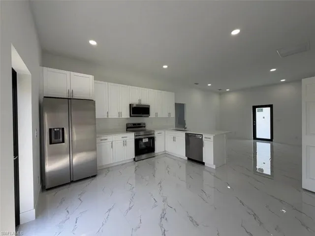 Modern kitchen featuring white shaker cabinetry, stainless steel appliances, a center island, and marble-look tile flooring