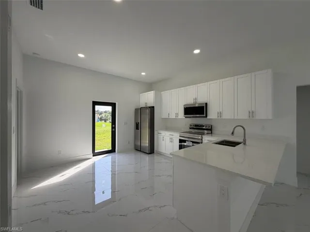 Open-concept kitchen featuring white shaker cabinetry, stainless steel appliances, and a central island with an undermount sink