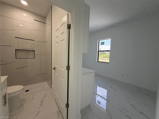 Modern bathroom featuring a walk-in shower with a built-in niche, white tile flooring with dark veining, a white toilet, and a vanity with a white countertop