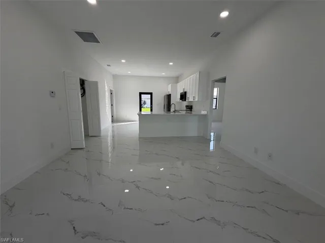 Spacious interior featuring large format marble-look tile flooring, recessed lighting, white walls, white baseboards, and a kitchen with white cabinetry and a white island