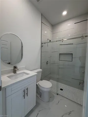 Contemporary bathroom featuring a frameless glass shower enclosure with a recessed niche, white vanity with a light-colored countertop, and a circular wall-mounted mirror