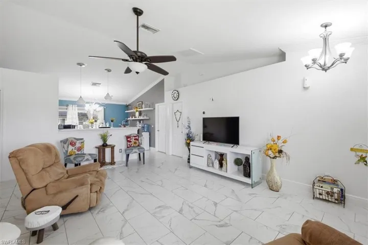 Vaulted ceilings highlight the spacious living area featuring large format tile flooring, a contemporary ceiling fan, and a chandelier