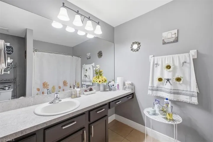 Bathroom featuring a single basin vanity with a light-toned countertop, dark wood-finish cabinetry, and a large wall-mounted mirror
