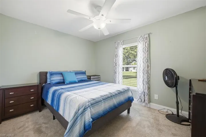 Carpeted bedroom featuring a ceiling fan, light green wall paint, a window with horizontal blinds, and baseboard trim