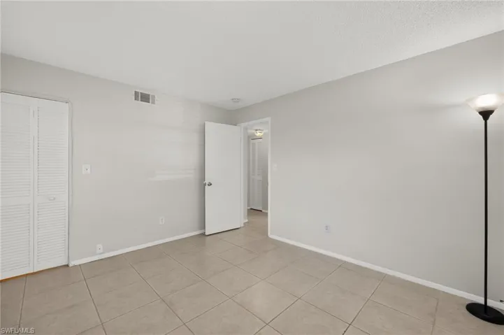 Unfurnished bedroom with light tile patterned floors, visible vents, baseboards, and a textured ceiling