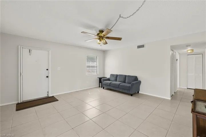 Living area featuring visible vents, a ceiling fan, a textured ceiling, light tile patterned flooring, and baseboards