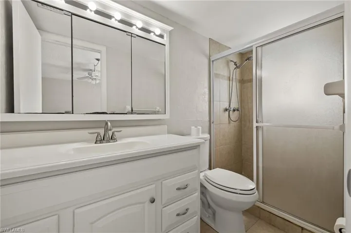 Bathroom featuring toilet, a stall shower, a textured wall, tile patterned floors, and vanity