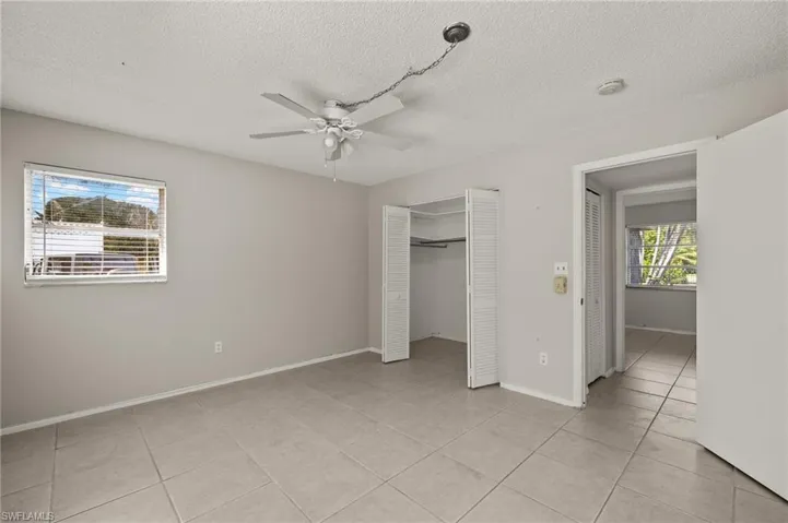 Unfurnished bedroom with a ceiling fan, a textured ceiling, a closet, light tile patterned flooring, and baseboards