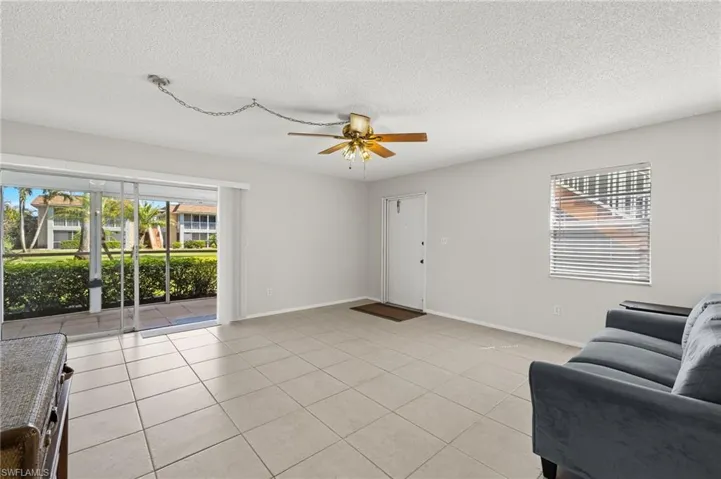 Living room with light tile patterned floors, a textured ceiling, baseboards, and a ceiling fan