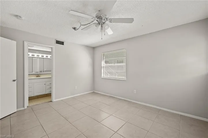 Unfurnished bedroom with light tile patterned floors, baseboards, visible vents, ceiling fan, and a textured ceiling