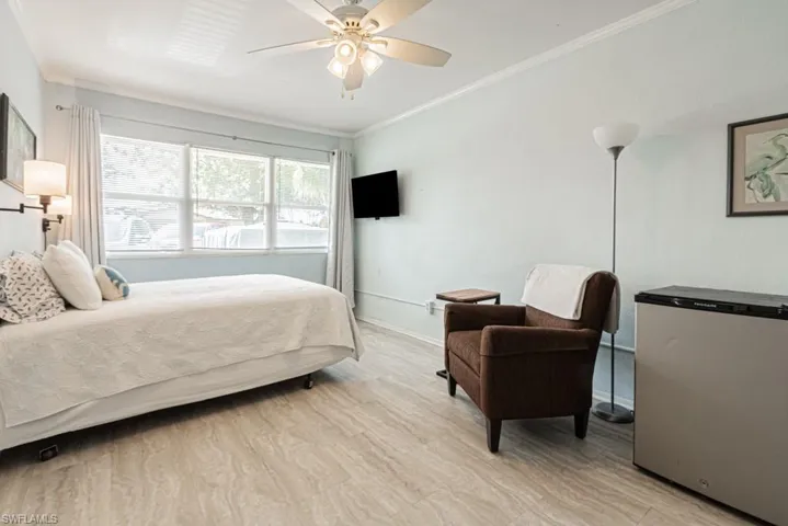 Bedroom featuring refrigerator, ornamental molding, light wood-type flooring, and ceiling fan