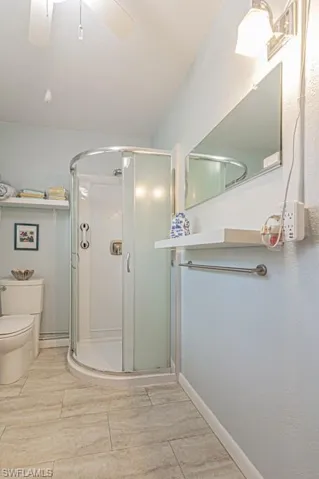 Bathroom with tile patterned floors, toilet, a shower with door, and ceiling fan