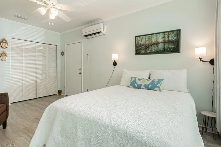 Bedroom with a closet, ceiling fan, a wall unit AC, ornamental molding, and light hardwood / wood-style flooring