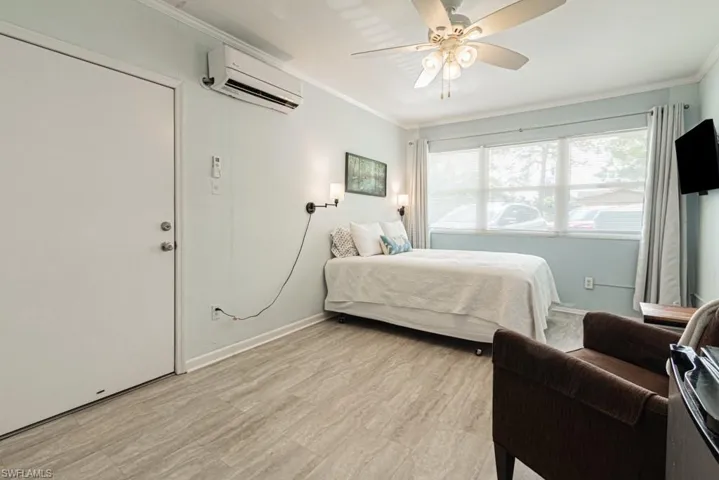 Bedroom with an AC mini split wall unit, ceiling fan, light wood-type flooring, and crown molding