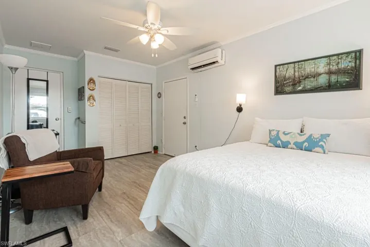 Bedroom with a wall unit AC, light hardwood / wood-style flooring, ceiling fan, and crown molding