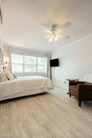 Bedroom with light hardwood / wood-style floors, crown molding, and ceiling fan