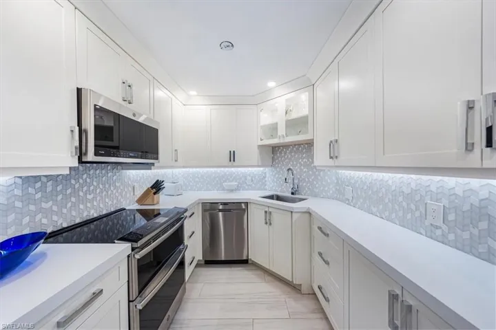 Kitchen featuring stainless steel appliances, tasteful backsplash, light countertops, white cabinetry, and glass insert cabinets