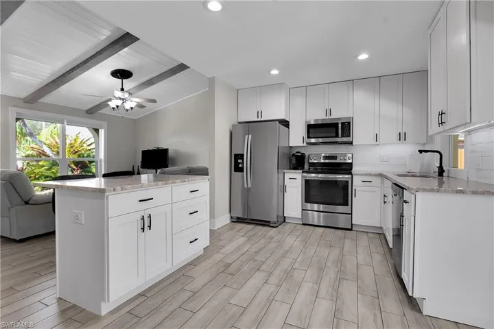 Kitchen with stainless steel appliances, light stone countertops, white cabinetry, open floor plan, and wood finish floors