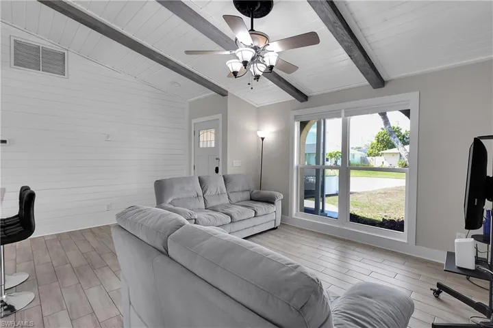 Living room with wood tiled floors, wooden walls, ceiling fan, lofted ceiling with beams, and wood ceiling