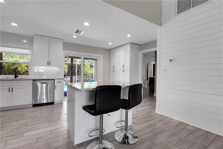 Kitchen with white cabinetry, wood tiled floors, stainless steel dishwasher, a kitchen breakfast bar, and recessed lighting