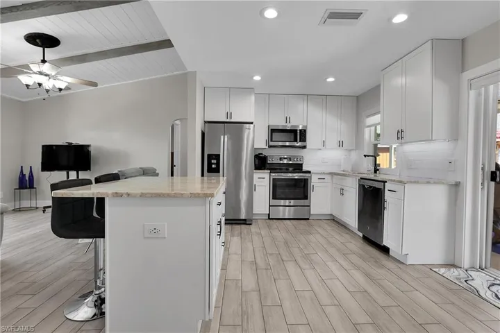Kitchen with stainless steel appliances, white cabinets, a kitchen island, a kitchen bar, and wood tiled floors